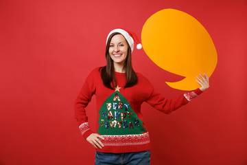 Joyful young Santa girl in Christmas hat holding yellow empty blank Say cloud, speech bubble isolated on red wall background. Happy New Year 2019 celebration holiday party concept. Mock up copy space.
