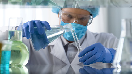 Scientist in protective goggles pouring acid liquid into vial, dangerous tests