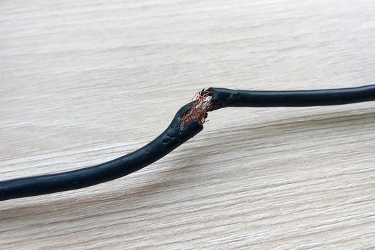 Damaged black electric cord on white background. Dangerous broken power electrical cable