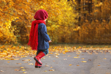 Happy autumn. Little girl laughs and runs in galoshes through the autumnal park.