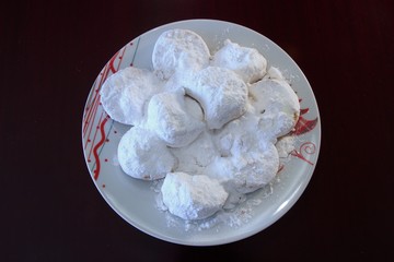 Qurabiya or kourambiethes is an almond flavoured crisp buns similar to macaroons it is a Greek traditional christmas dessert with powdered sugar on a white plate isolated on a black table