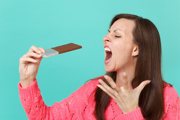 Crazy young woman in knitted pink sweater spreading hand, fingers holding biting chocolate bar...