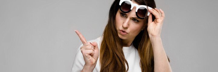 Portrait of emotional beautiful plus size model in sunglasses standing in studio looking in camera posing