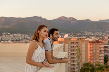 Fototapeta premium Young couple enjoying mountain and city view from rooftop terrac