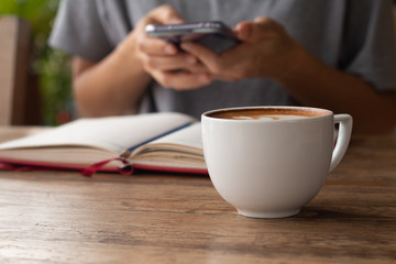 Woman checking her work on smart-phone blurred on background with warming drink, Late coffee in a cup in front-of on wooden table on-line working concept design
