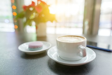 Winter background symbolic photo. Coffee shop, sparkling festoon, cup of coffee, macaroon on saucer, Red Christmas poinsettia flower
