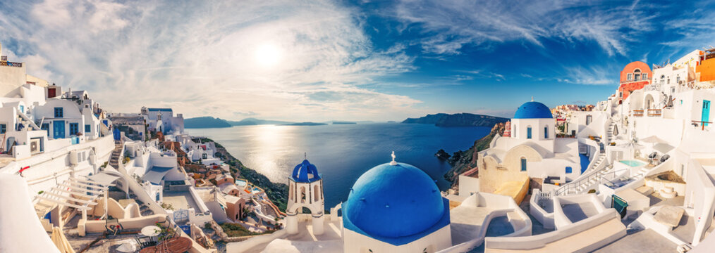 Fototapeta Churches in Oia, Santorini island in Greece, on a sunny day with dramatic sky. Panorama view.