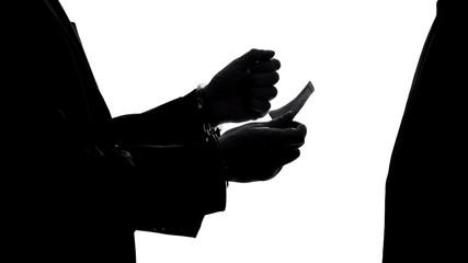 Criminal businessman in handcuffs giving bribe for prison release, corruption
