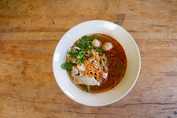 Rice noodle in spicy soup with pork ball, vegetable and pork serving on wooden desk in canteen