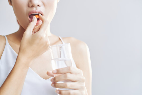 Woman taking daily vitamins with glass of fresh water
