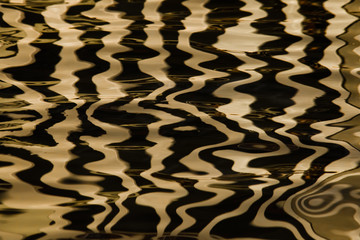 Waves on the water forming stripes similar to the texture of velvet, the alternation of gold and black stripes and waves.