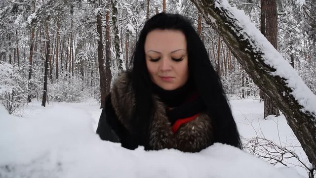 Portrait of a young girl in black clothes near a snow tree in the forest.