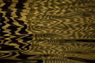Waves on water create freakish diffractional structures similar to velvet on its surface, yellow  reflections on water organized into strict and chaotic structures.