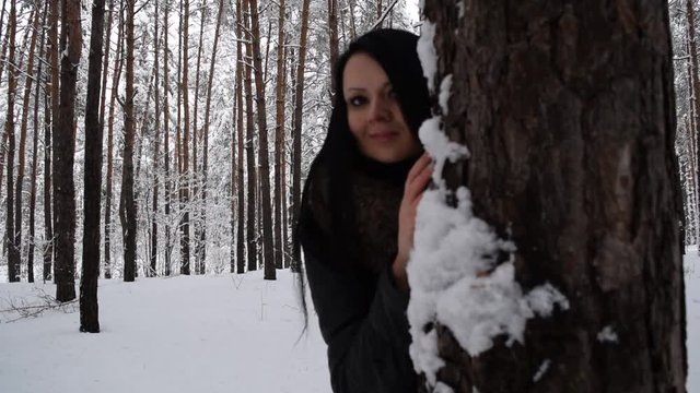 Young girl in black stands near pines in winter forest.