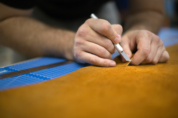Male hands cutting leather in a workshop, close up