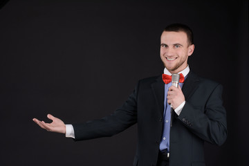 Handsome Master of ceremonies in black suit holding microphone in hand on black background....