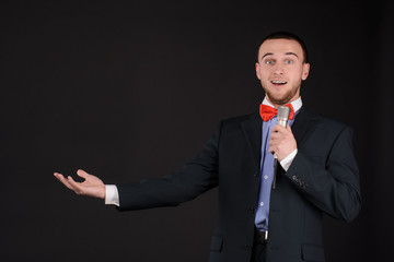 Surprised Handsome Master of ceremonies in black suit holding microphone in hand on black background. Showman, tv