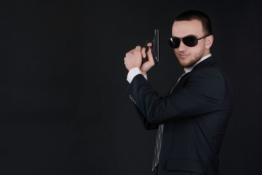 Man in black suit and sunglasses hold a gun in his hand. Prepearing to aim and shoot.