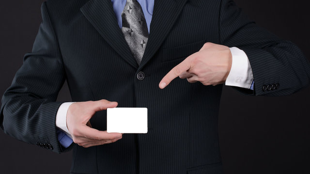 Man in suit holding business card by one hand and point pointing her with his index finger