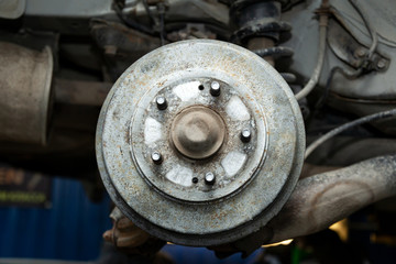 Close-up of heavily worn rear drum brakes on a car raised on a lift in a car repair shop