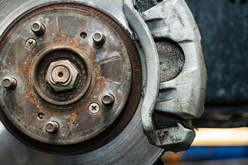 Close-up of the replacement of the old front brake disc, brake caliper and hub nut on a car lifted on a lift with the help of a pneumatic wrench in a car repair shop. Auto mechanic repair.
