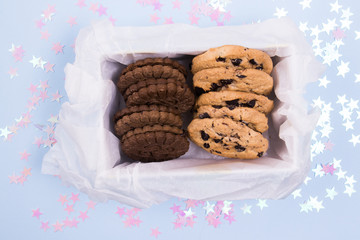 Tasty cookies in a box on a pastel blue background with pink stars confetti.