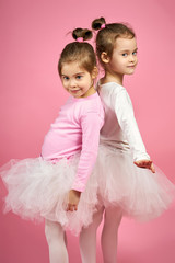 two cute little girls in white tulle skirts on a pink background