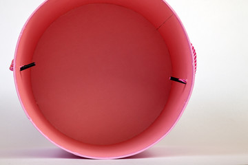 Top view of a pink pink round cardboard box empty inside for gift wrapping on a white background close-up and with a ribbon in the form of a pen on the side.