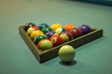 blurred multi-colored billiard balls with numbers lie in a wooden pyramid on a blue cloth table next to a white ball