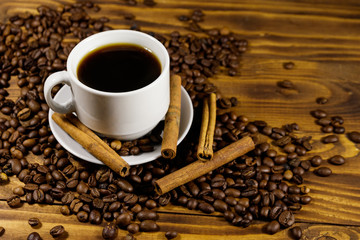 Cup of coffee, roasted coffee beans and cinnamon sticks on wooden table