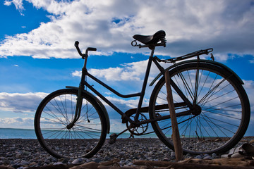 Classic (old) bicycle by the sea, blue sky with clouds, contrasting silhouette of a bicycle