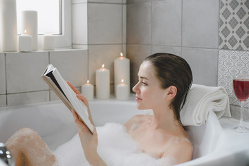 Young woman relaxes in a hot bath full of foam.
