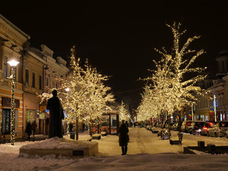 Shiny Christmas lights illuminate the snow covered trees along the promenade in the evening. Long...