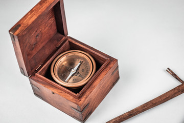Old historical rare nautical compass and pivot tool for measuring long distances at sea and essential orientation. Details of the wooden textured box and brass casing. White background, neutral light.
