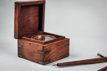 Old historical rare nautical compass and pivot tool for measuring long distances at sea and essential orientation. Details of the wooden textured box and brass casing. White background, neutral light.