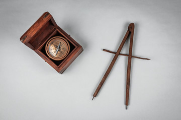 Old historical rare nautical compass and pivot tool for measuring long distances at sea and essential orientation. Details of the wooden textured box and brass casing. White background, neutral light.