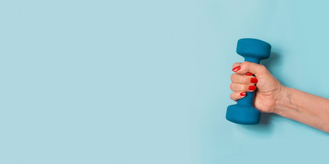 Female hand with blue dumbbell on blue. Sport concept. Wellness.