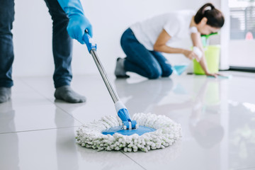 Housekeeping and cleaning concept, Young couple in blue rubber gloves wiping dust using mop and duster while helping cleaning on floor at home