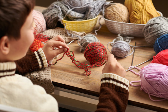 Child boy is learning to knit. Colorful wool yarns are on the wooden table. They are placed as smiling face. Hand closeup.