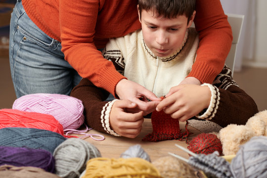 Mother is learning her child boy to knit. Colorful wool yarns are on the wooden table.