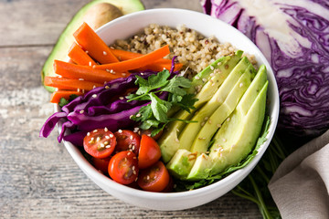 Vegan Buddha bowl with fresh raw vegetables and quinoa on wooden table. Close up