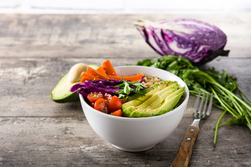 Vegan Buddha bowl with fresh raw vegetables and quinoa on wooden table. 