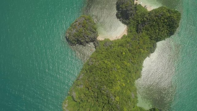 Aerial view of island Kagbalinad with sand beach and turquoise water in blue lagoon among coral reefs, Caramoan Islands, Philippines. Mountains covered with tropical forest.