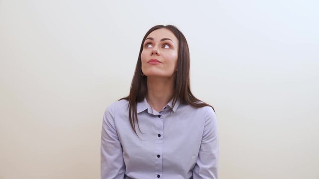 A pretty long-haired brunette sitting and wiggling, she looks to the right, up, twists lips and looks in front of her. She sighs and looks down with a pensive look