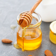 Honey background. Sweet honey in glass jar with almonds. On gray background.