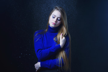 Beautiful, young girl with blond hair in a blue sweater on a snowfall in winter