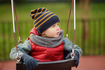 Cute little boy having fun on outdoor playground. Child on swing