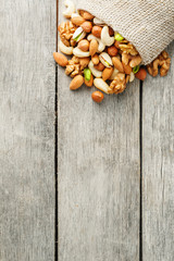 Mix of different nuts in a wooden cup against the background of fabric from burlap. Nuts as structure and background, macro. Top view.