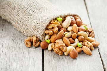 Mix of different nuts in a wooden cup against the background of fabric from burlap. Nuts as structure and background, macro. Top view.
