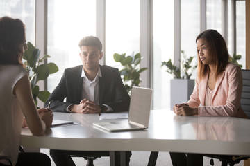 Multi-ethnic millennial people negotiating in boardroom. Caucasian biracial females Arabian male businesspeople sitting at office desk discussing in modern conference room share information and ideas